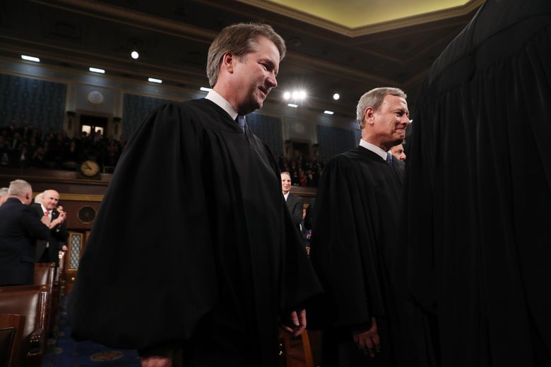 Brett Kavanaugh and John Roberts stand while wearing robes.